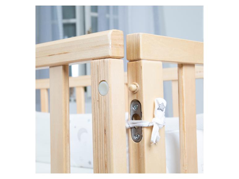 Gros plan d'un lit bébé en bois avec une protection blanche et une décoration en forme d'étoile.