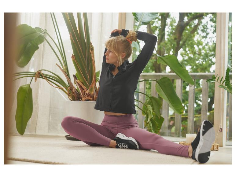 Vrouw in zwart sportjack en paarse legging rekt zich binnen uit.