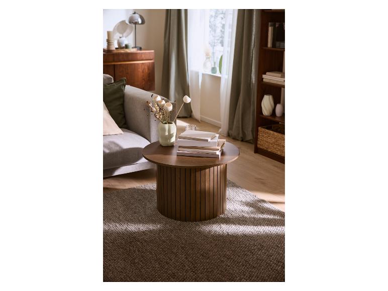 Table basse ronde en bois avec livres et vase dans le salon.