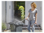 Een vrouw maakt een vuilnisbak schoon met een tuinslang.