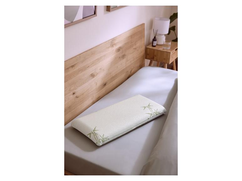 Oreiller blanc à motif bambou sur un lit avec tête de lit en bois et table de chevet.
