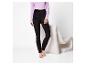 Femme en leggings noirs et haut violet, debout à côté d'un fauteuil blanc.