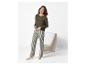 Femme souriante en pyjama rayé vert, debout à côté d'une chaise blanche.