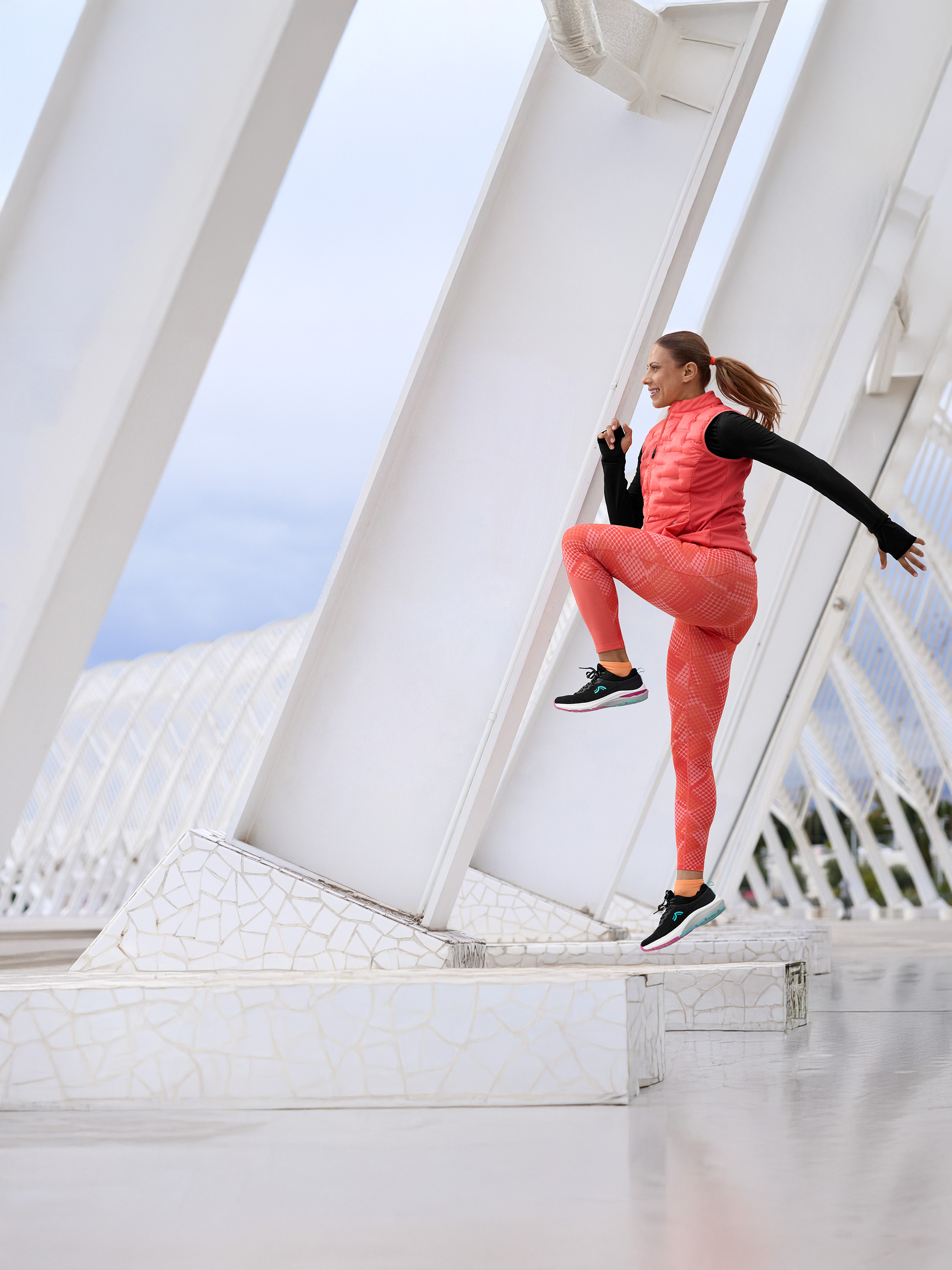 Vrouw in koraal en zwarte sportkleding, oefenend op een moderne witte structuur.