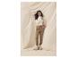 Femme en pantalon marron et chemisier blanc, avec bottes et sac beiges.