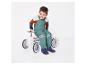 Un enfant en salopette verte et bottes bleues est assis sur une voiture jouet blanche.