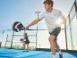 Man in wit sportshirt en donkere shorts speelt padel met een racket.