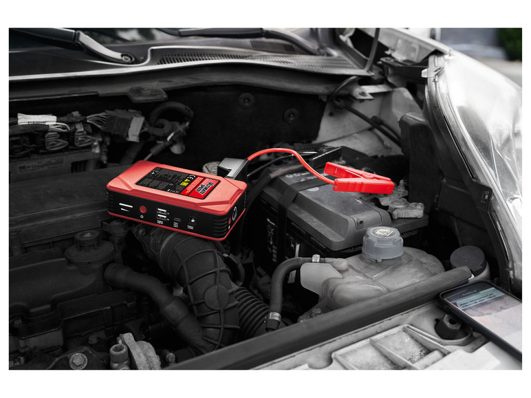 Een rode Jump Starter van het merk Ultimate Speed in de motorruimte van een auto.