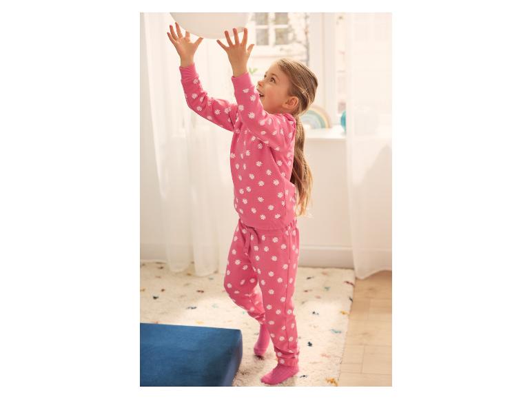 Fille en pyjama rose à imprimé marguerites jouant avec un ballon blanc à l'intérieur.