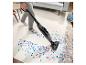 Un aspirateur balai nettoie des confettis colorés sur un tapis beige dans un salon.