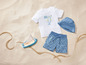 Un short de bain, un t-shirt avec un imprimé de poisson et une casquette bleue sur le sable.