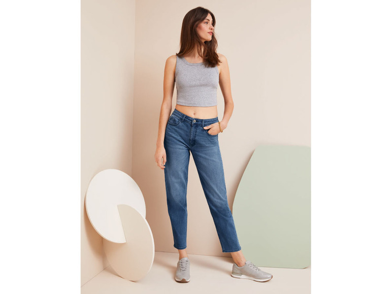 Een vrouw draagt een grijze tanktop en blauwe jeans.
