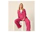 Lachende vrouw in fuchsia overhemd en wijde broek, zittend op een wit blok.