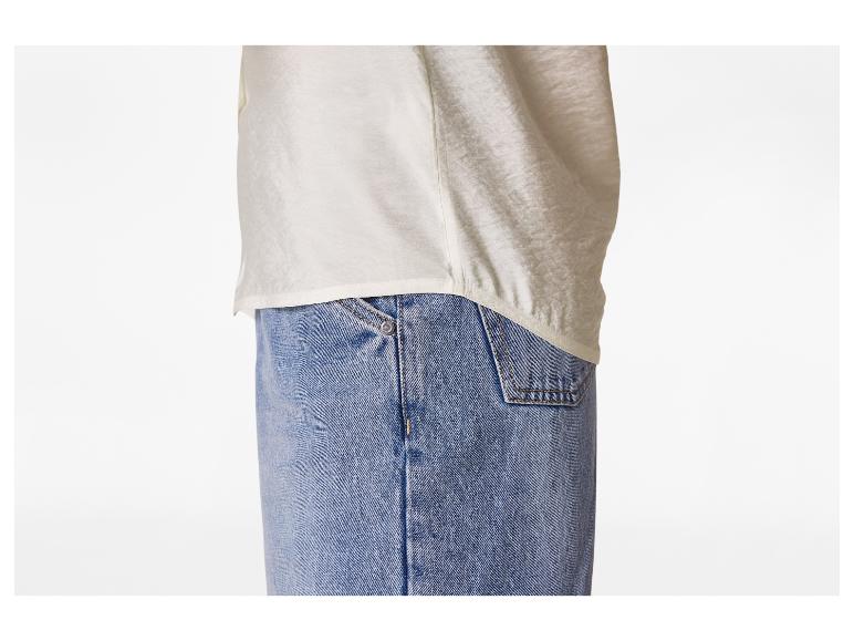 Witte blouse en blauwe jeans, met zichtbare stiksels en een metalen klinknagel.