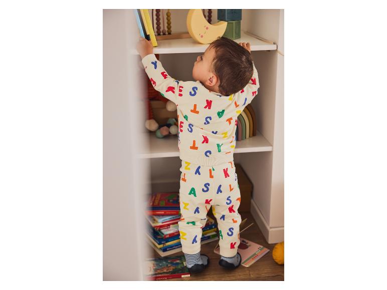 Un jeune enfant en pyjama à lettres prend des livres sur une étagère.