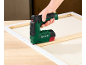 Een hand gebruikt een elektrische tacker om canvas aan een houten frame te bevestigen.