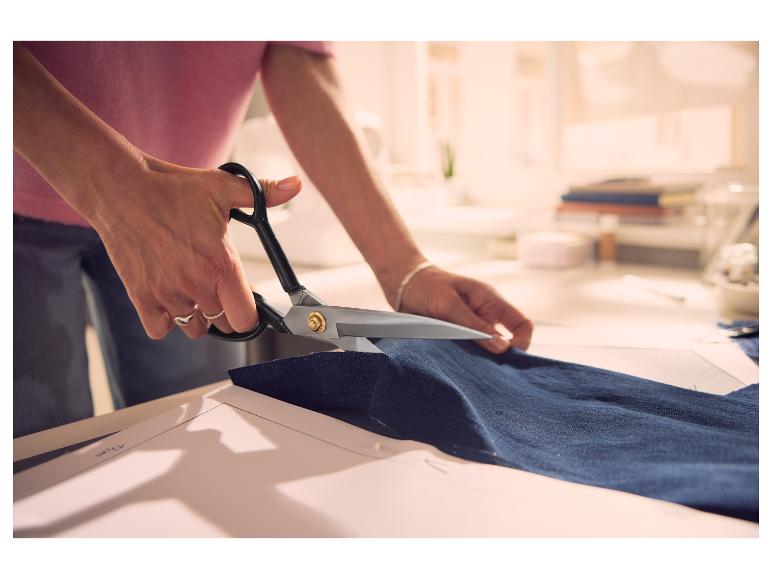 Kleermakersschaar die blauwe denimstof knipt op een werktafel.
