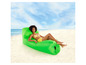 Een vrouw die op een opblaasbaar groene loungestoel ligt op het strand.