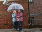 Deux enfants en vêtements de pluie sous un parapluie transparent.