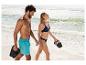 Paar in zwemkleding en slippers loopt lachend over het strand.