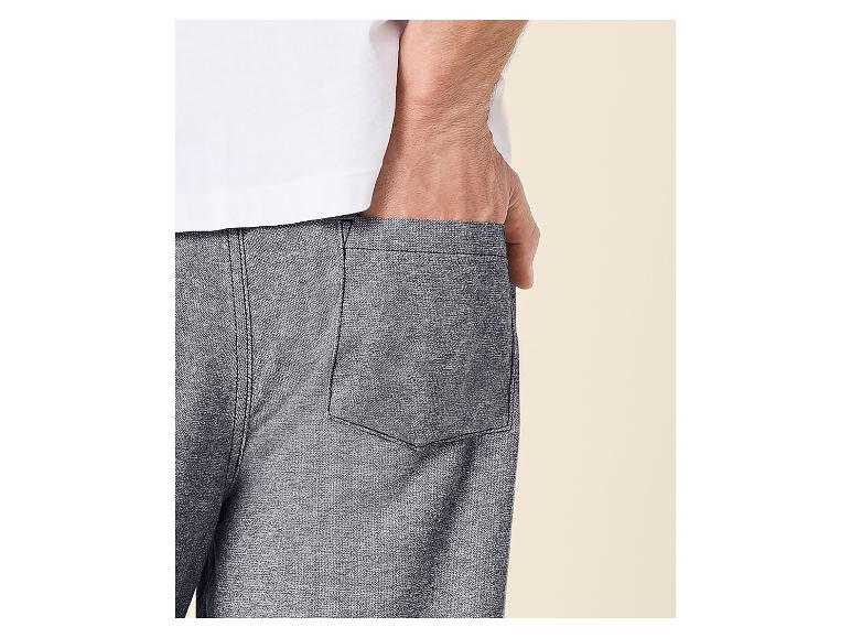 Homme en t-shirt blanc et short gris, la main dans la poche.
