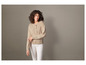 Een vrouw draagt een beige trui en witte broek.