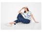 Vrouw in gestreept poloshirt, wijde jeans en baseballpet, zittend en lachend.