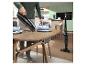 Homme utilisant un aspirateur balai pour nettoyer les miettes d'une table en bois dans une cuisine.