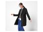 Une femme présente un manteau noir mi-long porté sur un pull gris et un jean bleu.
