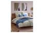 Slaapkamer met houten bed, bloemendekbedovertrek, blauwe kussens en abstracte muurkunst.