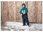 Een kind in een blauwe winteroverall staat op een houten vloer met kunstmatige sneeuw.