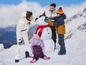 Une famille construit un bonhomme de neige dans les montagnes.