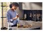 Femme mixant des ingrédients verts avec un mixeur plongeant dans une cuisine moderne.