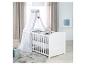 Lit bébé blanc avec baldaquin, ours en peluche gris et tapis dans une chambre d'enfant.
