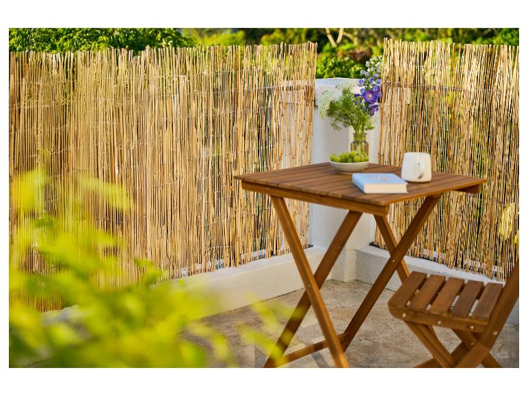 Bamboe schutting op balkon met houten tafel en stoel, bloemen en boek.