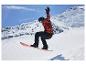 Snowboarder en veste rouge et noire, pantalon noir, casque et lunettes, en plein saut.