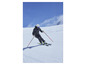 Un skieur en veste grise et casque descend une pente enneigée.