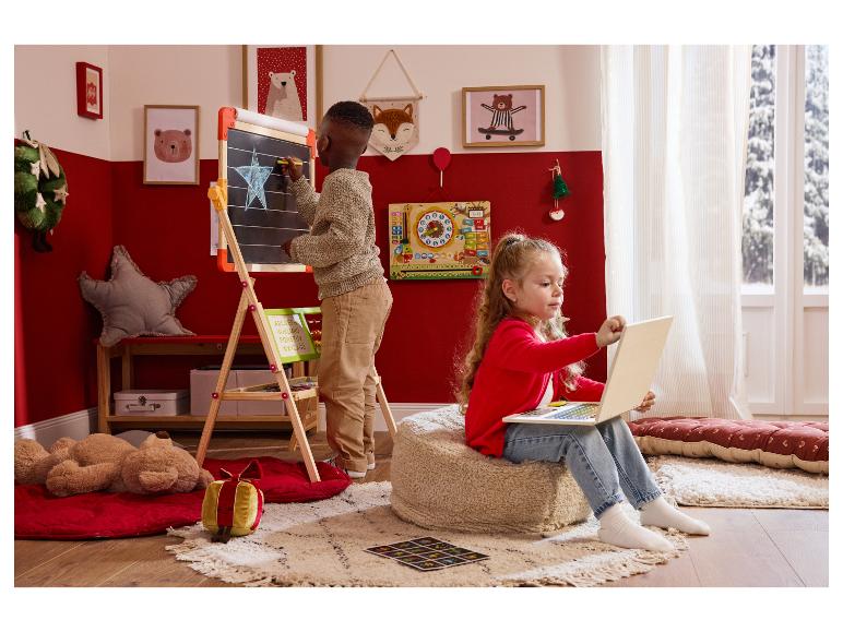 Twee kinderen spelen in een kerstversierde kamer: een jongen tekent op een schoolbord, een meisje gebruikt een laptop.