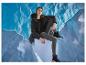 Femme en veste noire et leggings gris, assise sur un cube bleu, sur fond bleu.