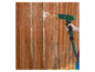 Een groene Parkside watersproeier sproeit water op een houten schutting.