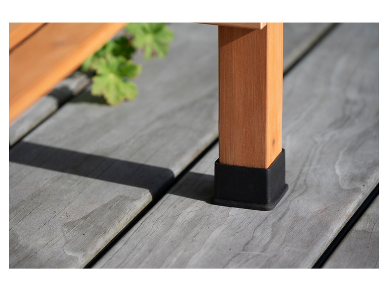 Een houten tafelpoot met een zwarte beschermkap op een houten terras.