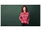 Une femme porte un pull rouge à motifs de Noël devant un fond vert.