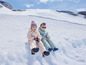 Deux enfants en vêtements d'hiver assis sur une colline enneigée.