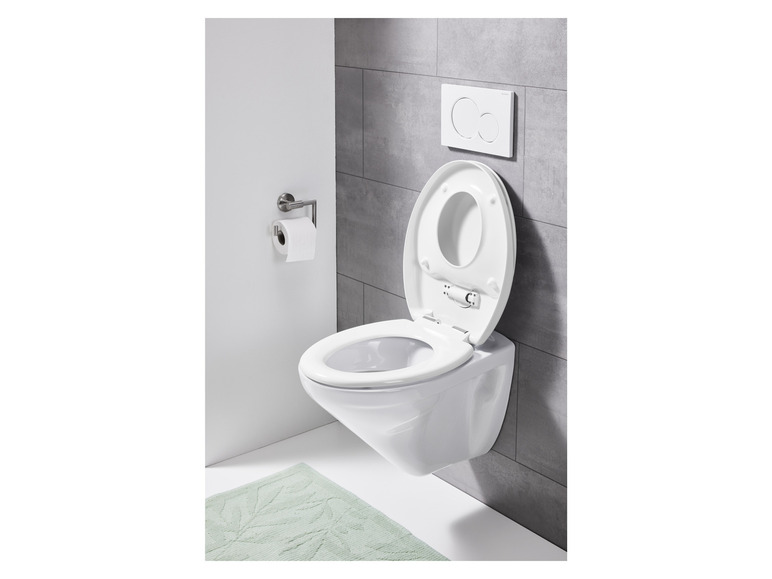 Een wit toilet met een softclose toiletbril, een Grohe inbouwreservoir en een groene badmat.