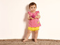 Une petite fille avec un haut rose et un short jaune tenant un ballon rose.