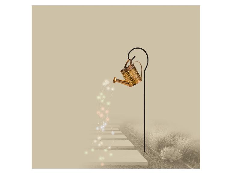 Arrosoir décoratif avec guirlande lumineuse, éclairant un chemin de jardin.