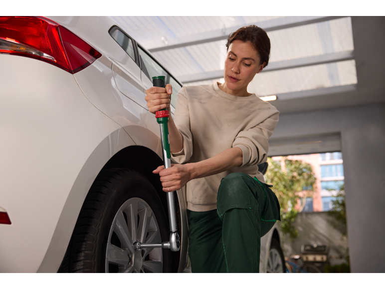 Vrouw verwisselt een autoband met een kruissleutel in een garage.