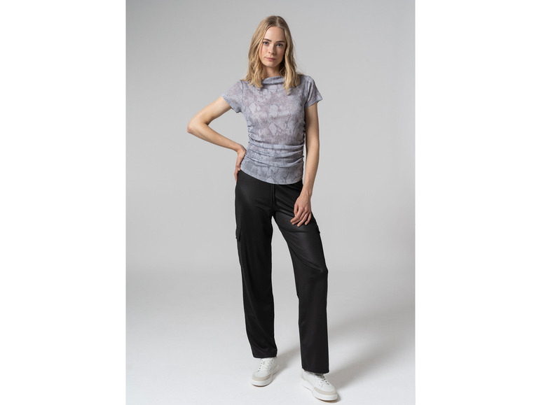 Een vrouw draagt een lichtgrijze blouse met luipaardprint en zwarte broek.