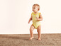 Een baby die op een vloerkleed staat in een gestreept rompertje.