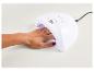 Une main aux ongles rouge foncé sous une lampe UV blanche.